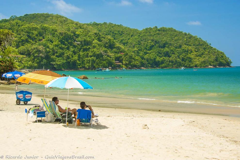 Imagem de dois amigos sentados em baixo de guarda sol curtindo a praia-Praia da Almada.